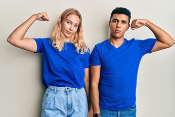 Young interracial couple wearing casual clothes strong person showing arm muscle, confident and...
