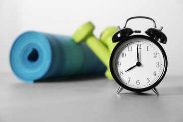 Alarm clock, yoga mat and dumbbells on grey background. Morning exercise