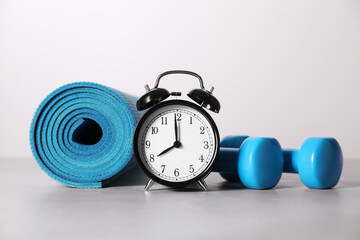 Alarm clock, yoga mat and dumbbells on grey background. Morning exercise