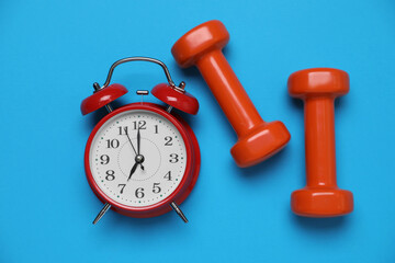 Alarm clock and dumbbells on light blue background, flat lay. Morning exercise
