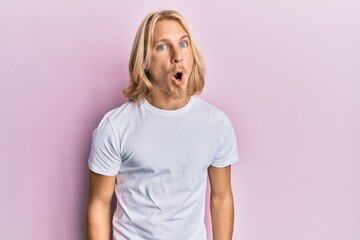 Caucasian young man with long hair wearing casual white t shirt afraid and shocked with surprise expression, fear and excited face.