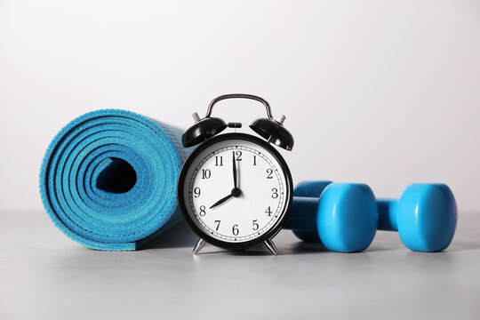 Alarm clock, yoga mat and dumbbells on grey background. Morning exercise