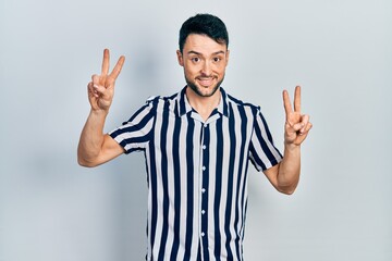 Young hispanic man wearing casual clothes smiling looking to the camera showing fingers doing victory sign. number two.