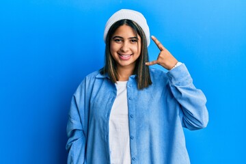 Young latin woman wearing cute wool cap smiling doing phone gesture with hand and fingers like talking on the telephone. communicating concepts.