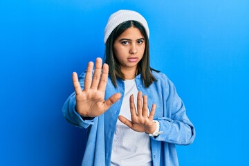 Young latin woman wearing cute wool cap moving away hands palms showing refusal and denial with...