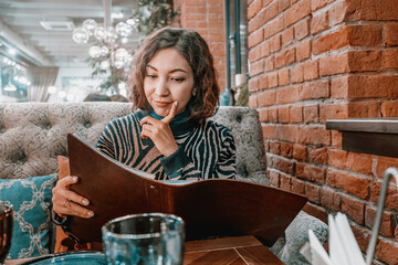 Happy woman chooses food and drinks from a large menu in a restaurant