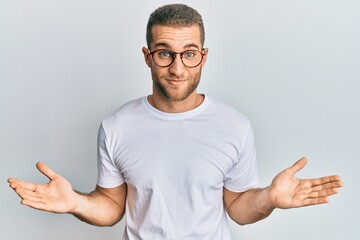 Fototapeta premium Young caucasian man wearing casual clothes and glasses clueless and confused expression with arms and hands raised. doubt concept.