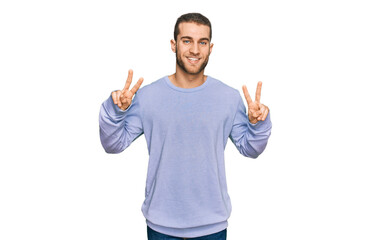 Fototapeta premium Young caucasian man wearing casual clothes smiling looking to the camera showing fingers doing victory sign. number two.