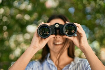 Young hispanic girl smiling happy using binoculars at the park.