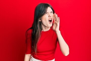 Young beautiful caucasian girl wearing casual red shirt shouting and screaming loud to side with hand on mouth. communication concept.