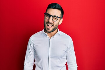 Young hispanic businessman wearing shirt and glasses winking looking at the camera with sexy expression, cheerful and happy face.