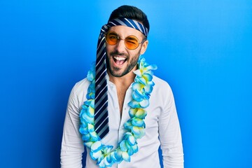 Young hispanic businessman wearing party funny style with tie on head winking looking at the camera...