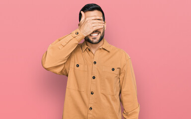 Young hispanic man wearing casual clothes smiling and laughing with hand on face covering eyes for surprise. blind concept.