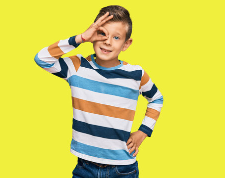 Adorable caucasian kid wearing casual clothes smiling happy doing ok sign with hand on eye looking through fingers