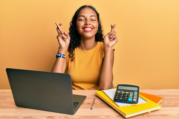 Young african american girl working at the office with laptop and calculator gesturing finger...