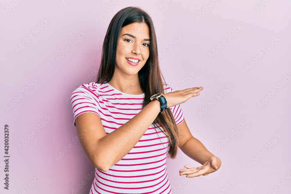 Canvas Prints Young brunette woman wearing casual clothes over pink background gesturing with hands showing big and large size sign, measure symbol. smiling looking at the camera. measuring concept.