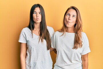 Hispanic family of mother and daughter wearing casual white tshirt making fish face with lips, crazy and comical gesture. funny expression.