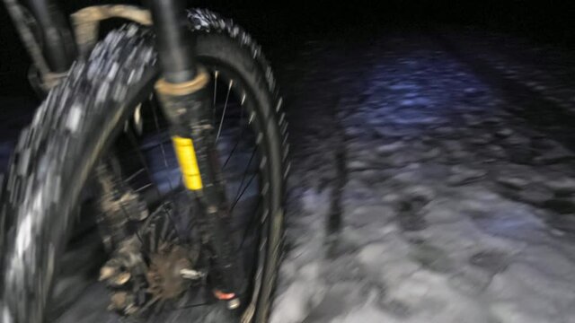 Low view of the front wheel of an mtb riding through a night snowy landscape.
