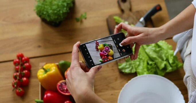 Woman taking photo of healthy salad with smartphone for her blog on kitchen at home, Food blogger concept, healthy lifestyle.