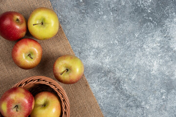 Wicker basket of ripe shiny apples on marble surface