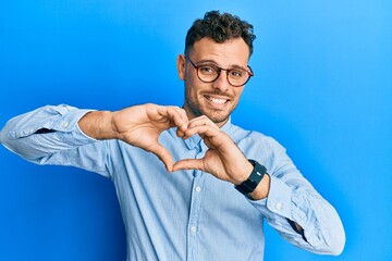 Young hispanic man wearing casual clothes and glasses smiling in love doing heart symbol shape with hands. romantic concept.