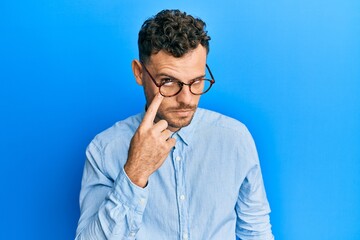 Fototapeta premium Young hispanic man wearing casual clothes and glasses pointing to the eye watching you gesture, suspicious expression