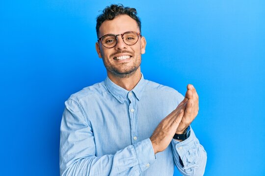 Young hispanic man wearing casual clothes and glasses clapping and applauding happy and joyful, smiling proud hands together