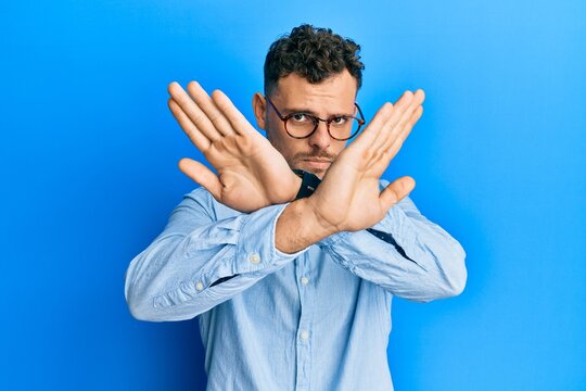 Young hispanic man wearing casual clothes and glasses rejection expression crossing arms doing negative sign, angry face