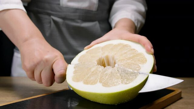Female hands cut pomelo in slices on cutting board. Close up, 150 fps