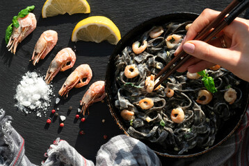 Fototapeta na wymiar black pasta and Shrimps with salt and lemon in a frying pan on a black background