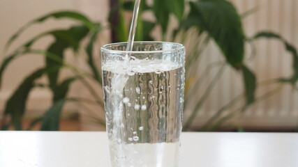 Drink water pouring in to glass at home over sunlight and natural green background on white table