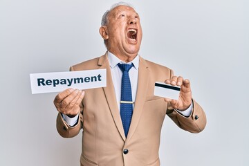 Senior caucasian man holding payment word paper and credit card angry and mad screaming frustrated and furious, shouting with anger looking up.