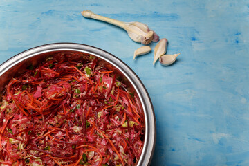 Metallic bowl of salad called Brush. Beetroot, carrots and cabbage cut into thin strips with garlic on blue wooden background. Vegetarian, organic, healthy food, diet, nutrition. Top view, copy space.