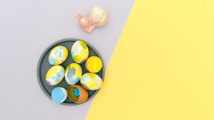 Top view of easter holiday yellow and gray backdrop with creative hand painted in trendy colors eggs set on concrete tray and cute bunny. Flat lay with space for text for postcard, banner, invitation