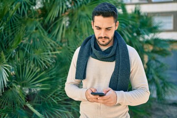 Fototapeta premium Young hispanic man with serious expression using smartphone at the park.