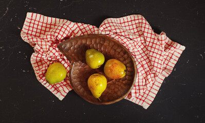 Top down view, green and yellow pears in wooden carved bowl, red chequered tablecloth and black...