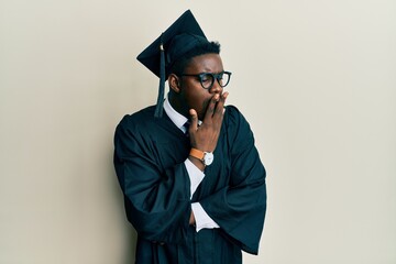 Handsome black man wearing graduation cap and ceremony robe bored yawning tired covering mouth with...