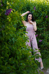 Beautiful dark-haired model posing among blossoming lilac bushes on spring background.