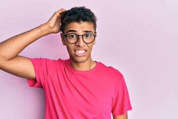 Young handsome african american man wearing glasses over pink background confuse and wonder about...