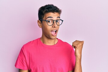 Young handsome african american man wearing glasses over pink background smiling with happy face looking and pointing to the side with thumb up.