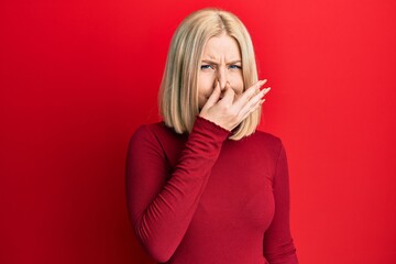 Young blonde woman wearing casual clothes smelling something stinky and disgusting, intolerable...