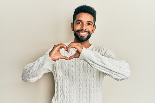 Handsome hispanic man with beard wearing casual winter sweater smiling in love doing heart symbol shape with hands. romantic concept.