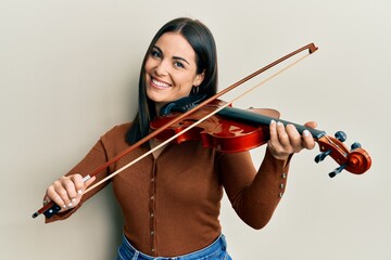 Young brunette woman playing violin smiling with a happy and cool smile on face. showing teeth.