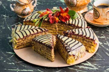 Sliced cake with cream, almonds, black and white chocolate on a wooden substrate on the table, a cup of coffee, close up copy space, holiday concept