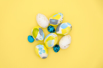 Top view of easter holiday yellow backdrop with creative eggs decorations in trendy blue, gray, golden colors. Flat lay colorful composition with copy-paste for text for postcard, banner, invitation