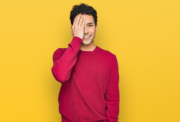 Young handsome man wearing casual clothes covering one eye with hand, confident smile on face and surprise emotion.