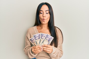 Young beautiful hispanic girl holding japanese yen banknotes making fish face with mouth and squinting eyes, crazy and comical.