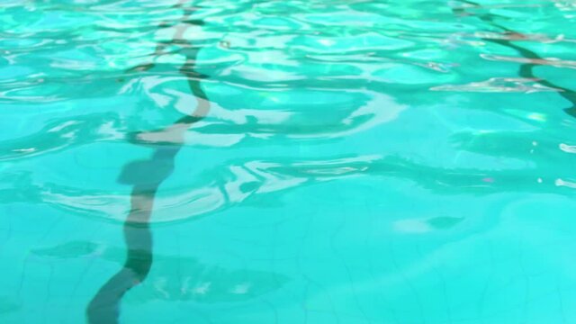 Water surface of swimming pool with small waves, dark lines visible on bottom