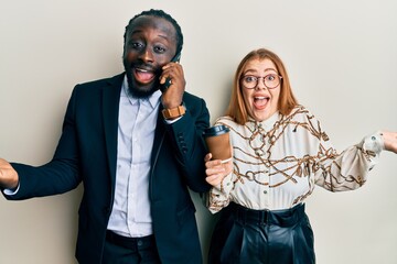 Young interracial couple using smartphone and drinking a cup of coffee celebrating achievement with happy smile and winner expression with raised hand