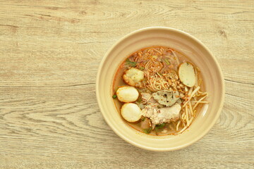 Chinese egg yellow noodles topping slice boiled pork and ball in spicy tom yum soup on bowl